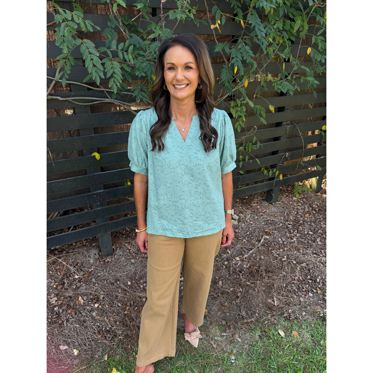 Annie Ks Boutique sage textured puff sleeve blouse paired with tan wide-leg trousers on a smiling woman outdoors
