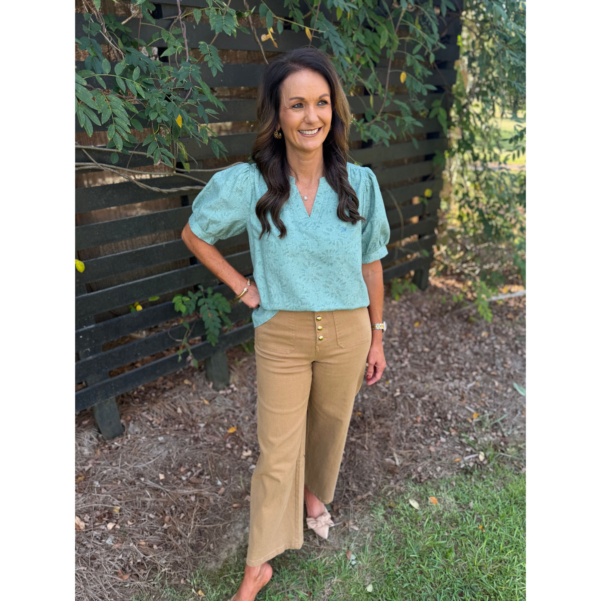 Annie Ks Boutique sage puff sleeve textured blouse paired with tan wide-leg trousers on a smiling woman outdoors