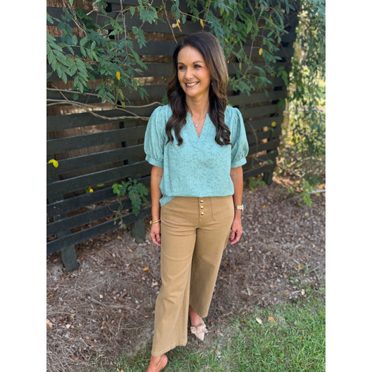 Annie Ks Boutique sage textured puff sleeve blouse paired with tan wide-leg trousers on a smiling woman outdoors.