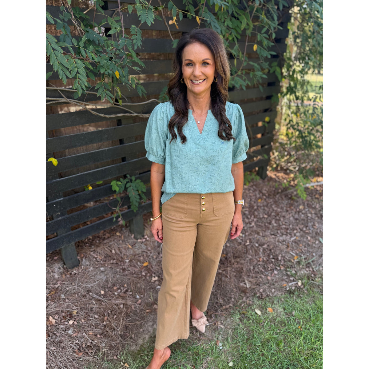 Annie Ks Boutique sage textured puff sleeve blouse paired with tan wide-leg trousers on a smiling woman outdoors