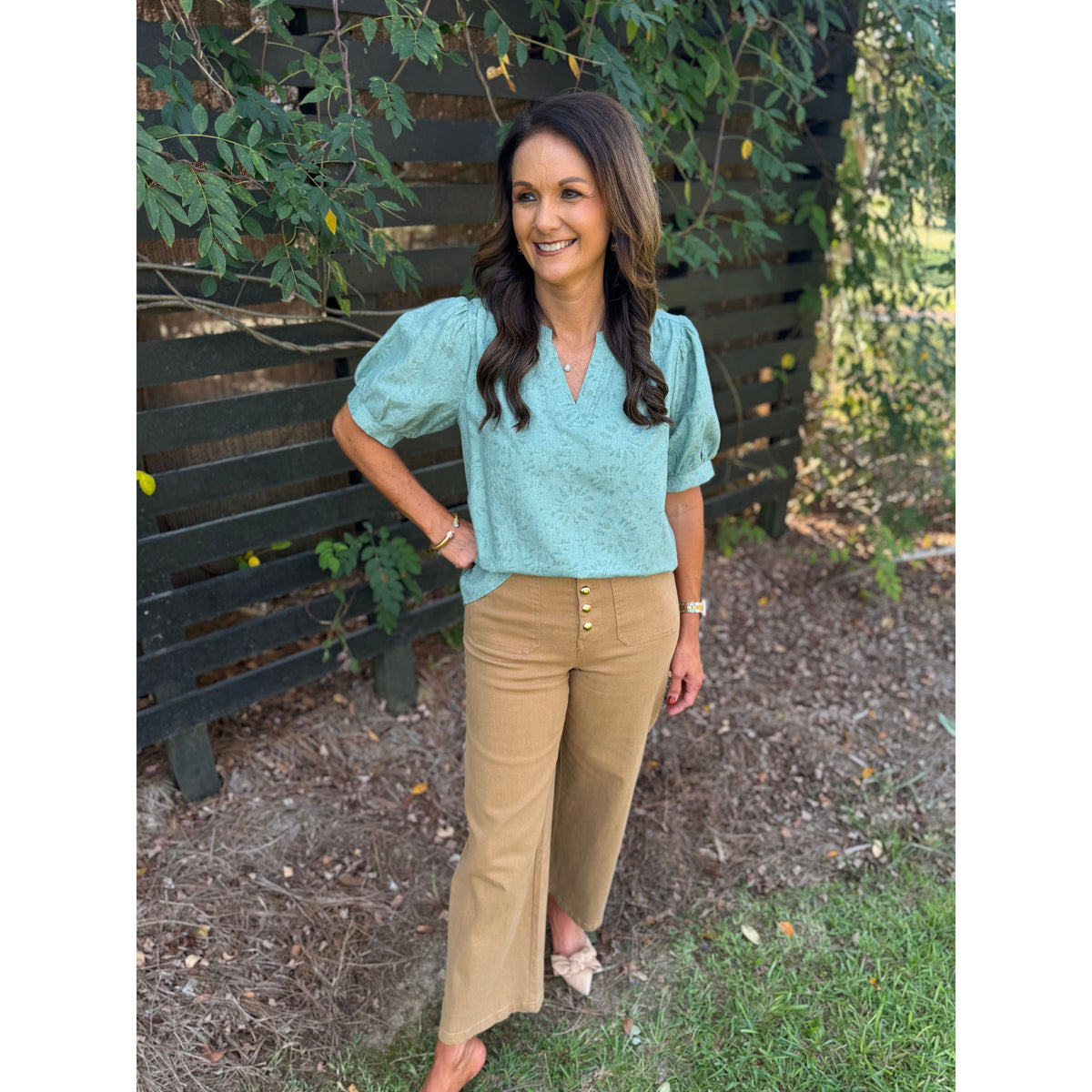 Annie Ks Boutique sage textured puff sleeve blouse paired with tan wide-leg trousers on a smiling woman outdoors