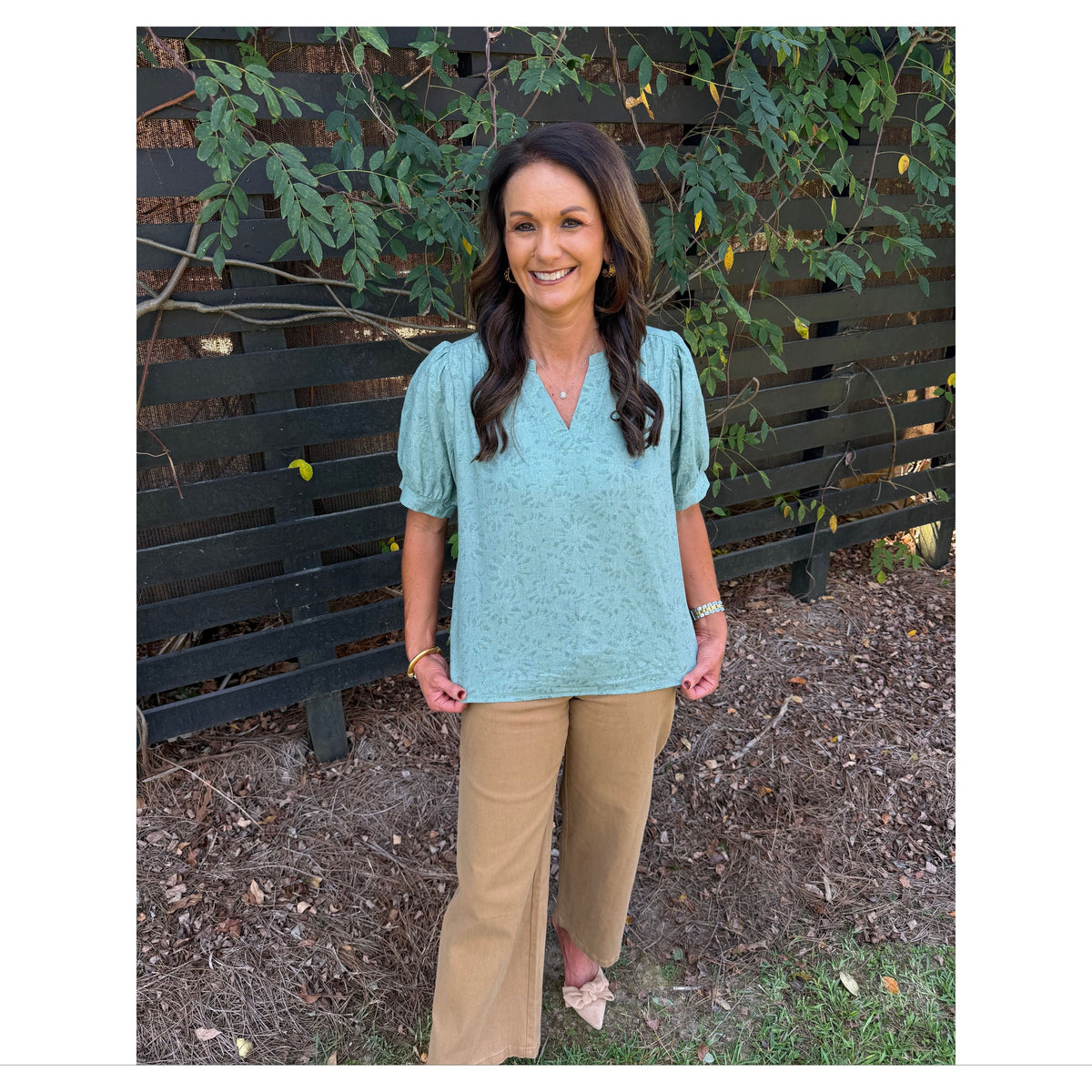 Annie Ks Boutique sage textured puff sleeve blouse with V-neckline worn with tan wide-leg trousers by a model