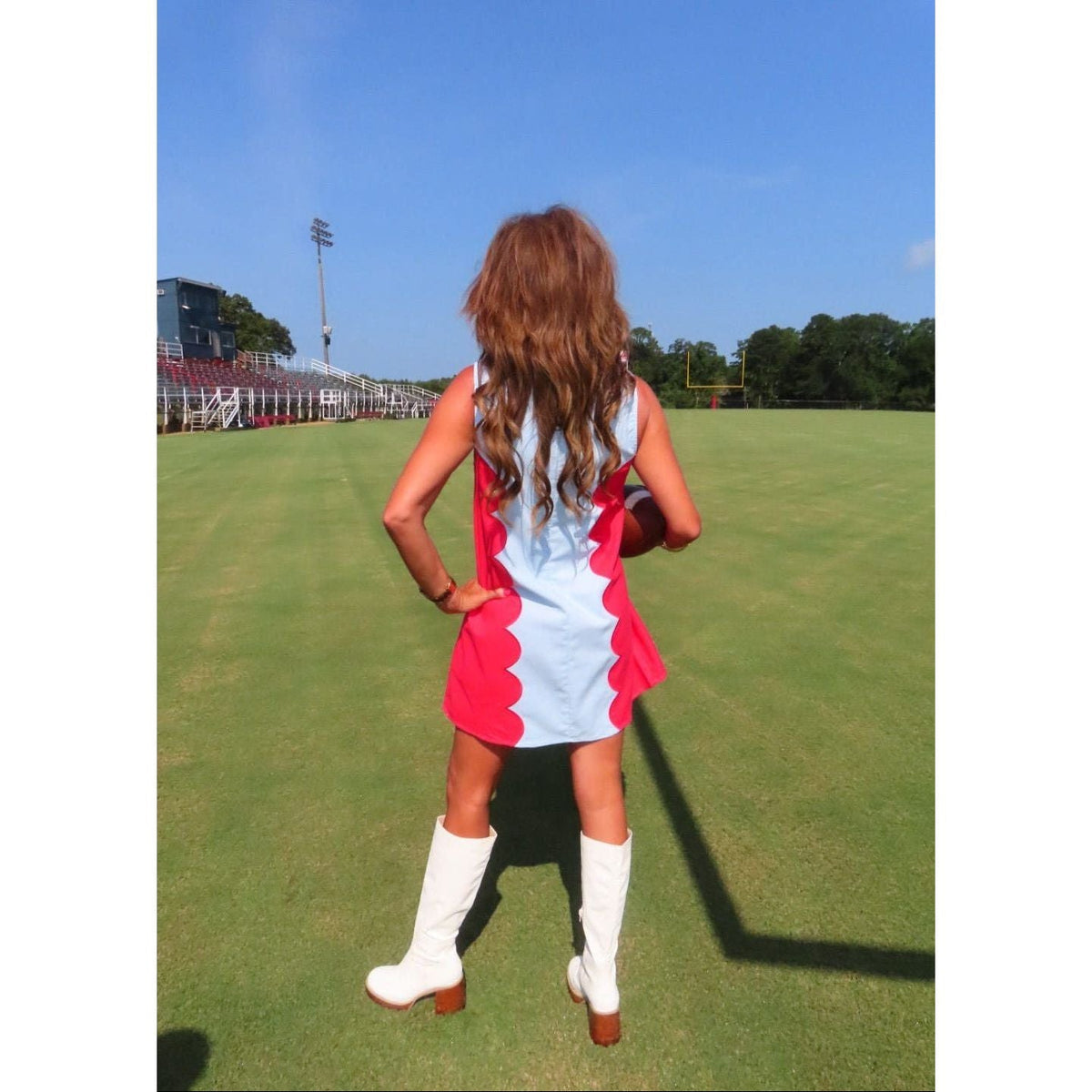Annie Ks Boutique red and powder blue scalloped sleeveless mini dress worn with white boots on a football field