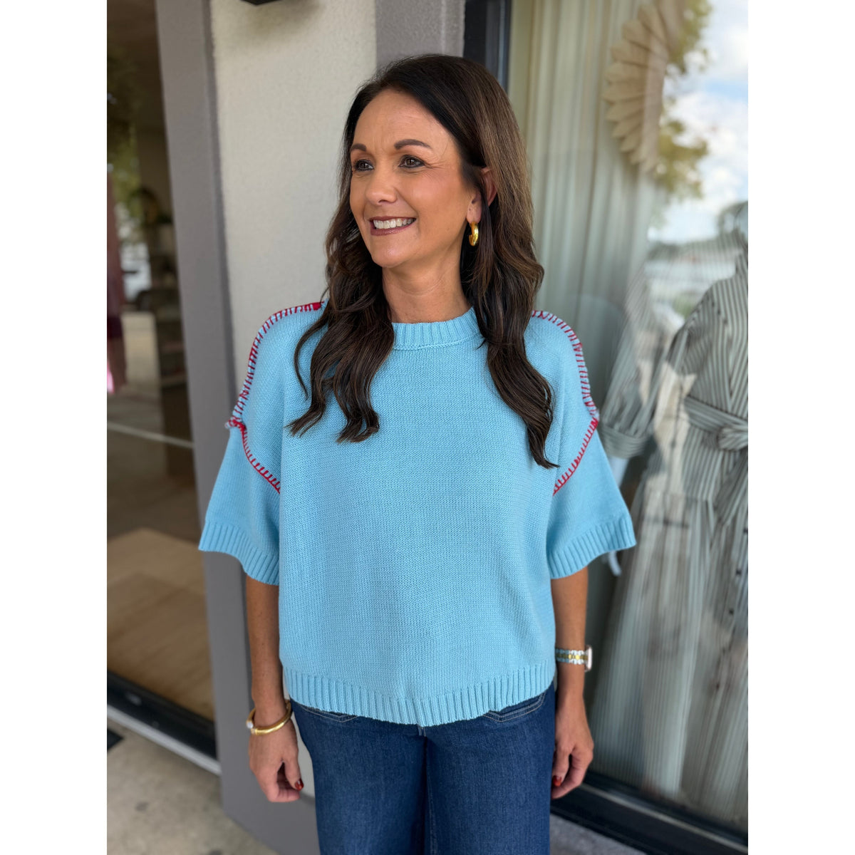 Annie Ks Boutique sky blue short sleeve sweater with red blanket stitch detail worn by a woman with dark hair