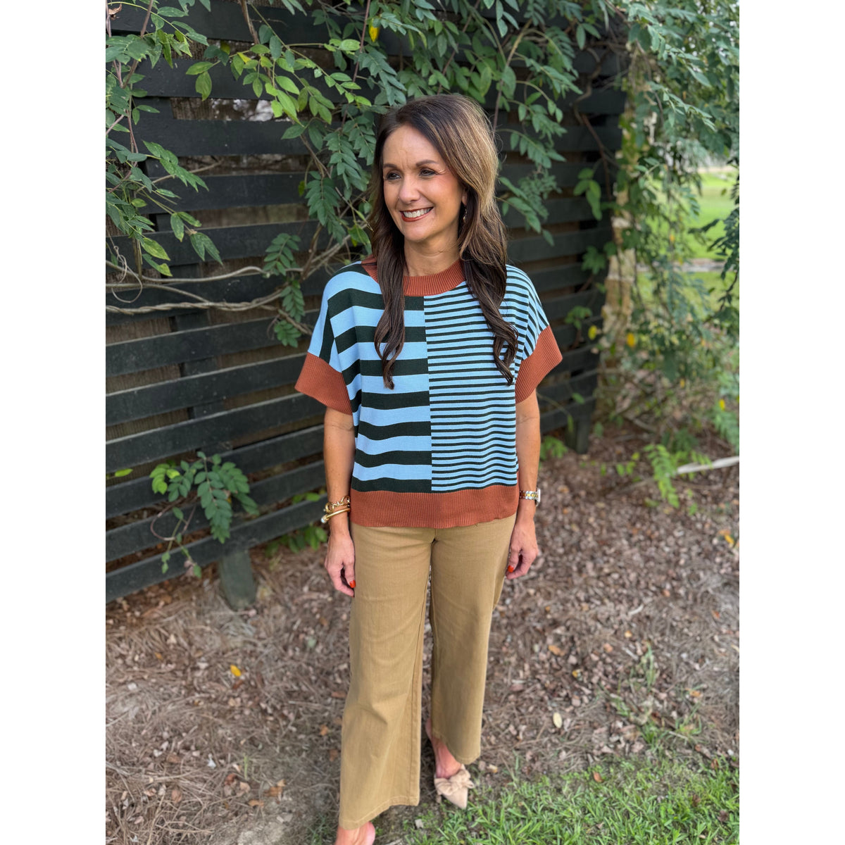 Annie Ks Boutique caramel and sea green striped drop-shoulder sweater worn with tan trousers in an outdoor setting.
