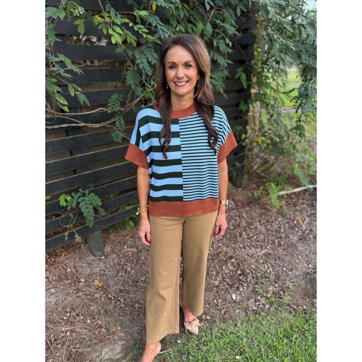 Annie Ks Boutique caramel and sea green striped drop-shoulder sweater worn with tan trousers in an outdoor setting.