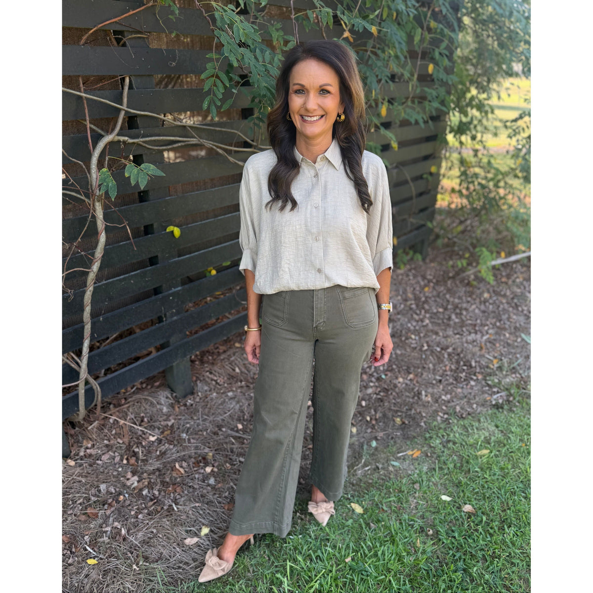 Annie Ks Boutique tan textured short sleeve button-front blouse worn with olive green trousers by a garden fence