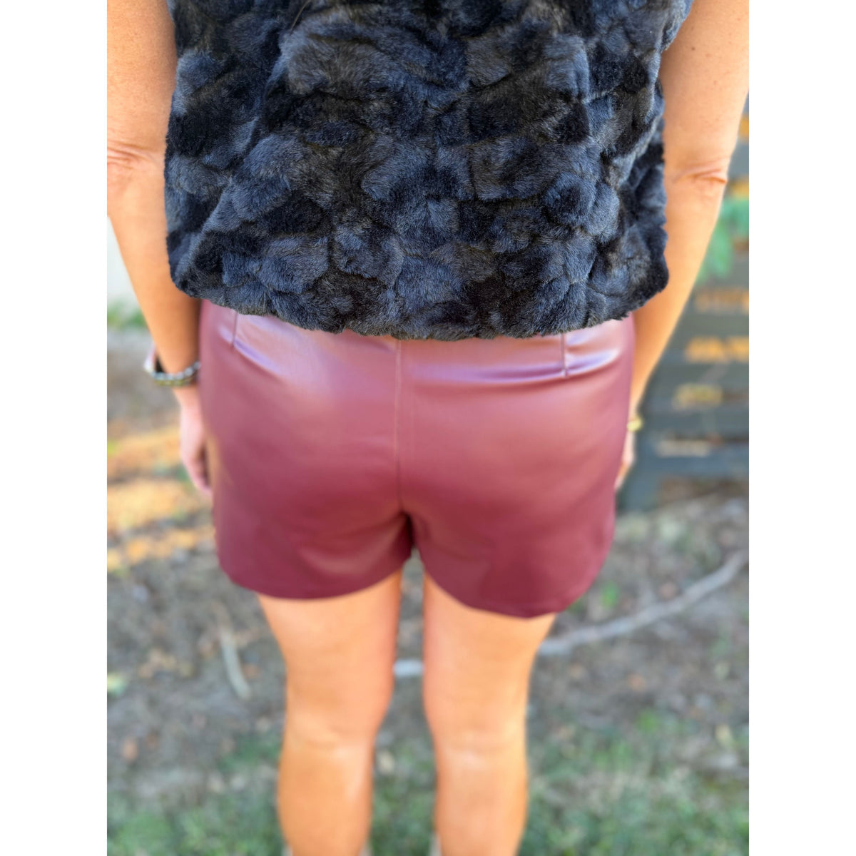 Annie Ks Boutique wine faux leather shorts with pintuck detail worn with a black faux fur vest, back view
