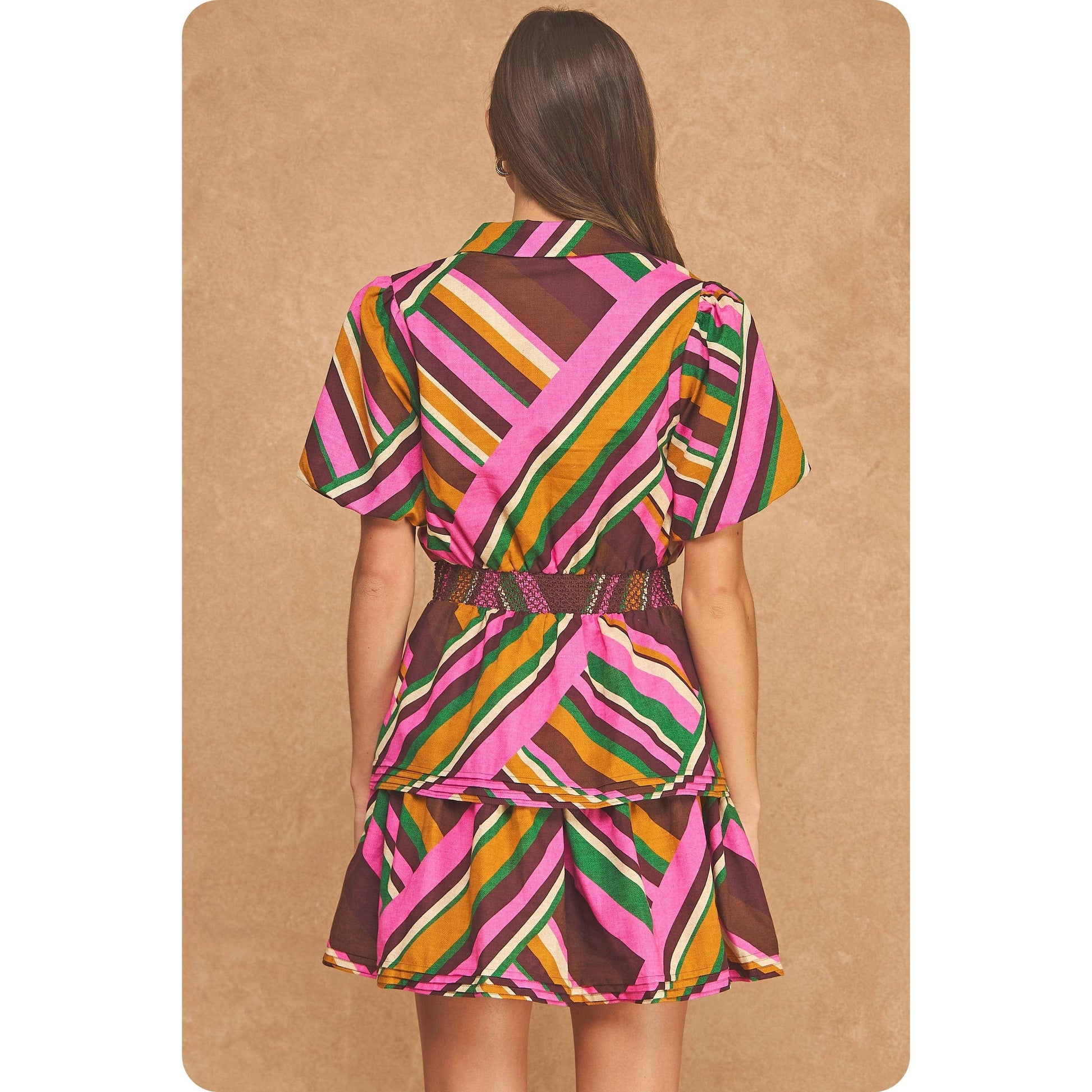 A woman shown from the back wearing a short-sleeve wrap-style dress with a colorful diagonal striped pattern in pink, brown, green, orange, and white, set against a textured tan background.