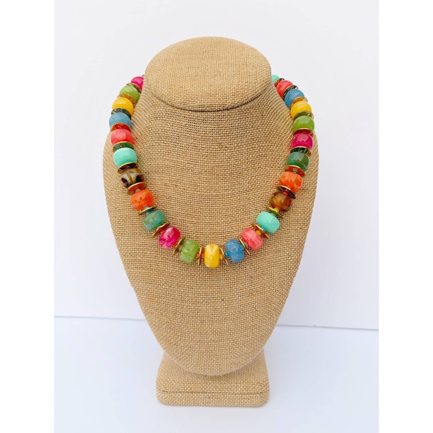 A colorful beaded necklace displayed on a tan burlap-covered jewelry bust against a plain white background.