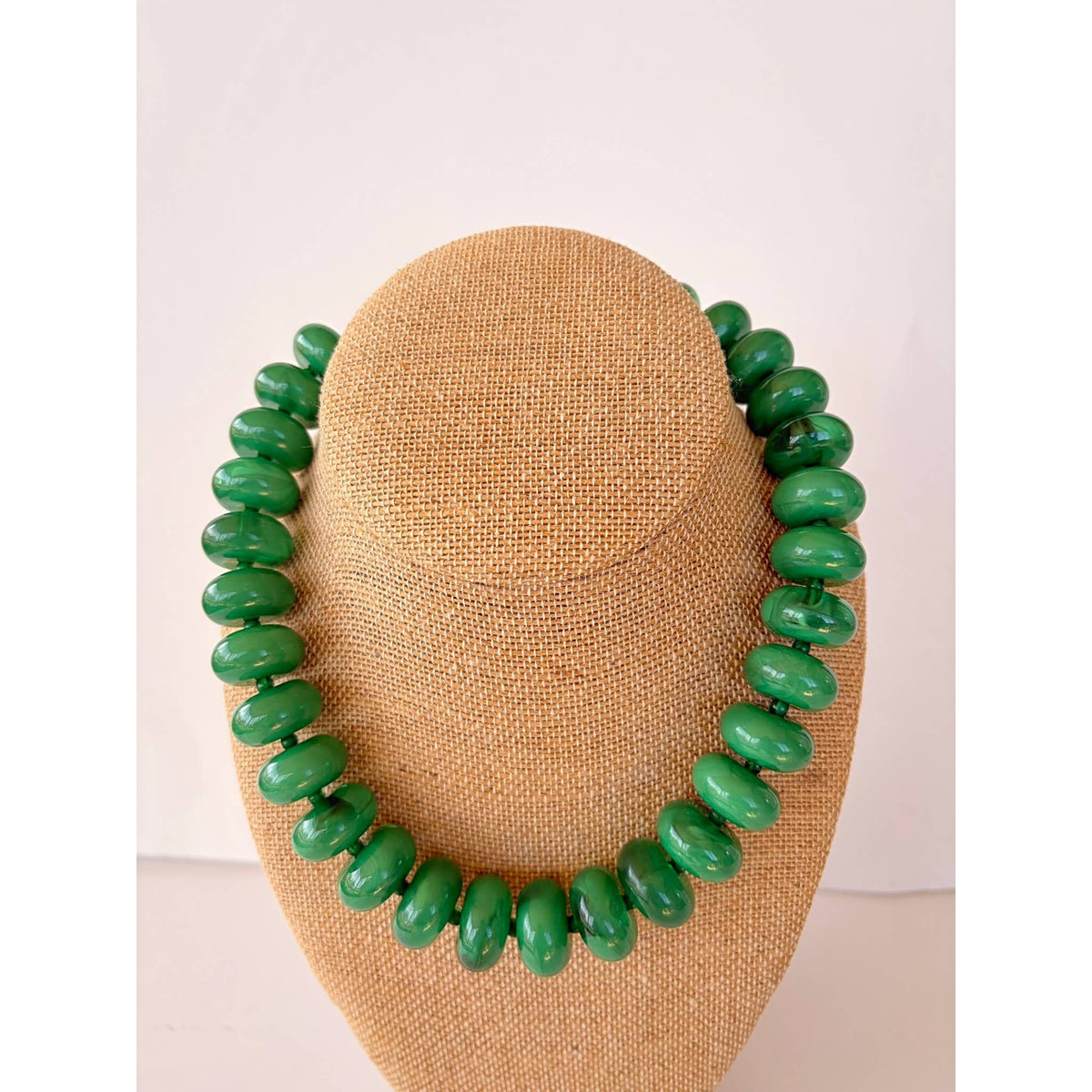 Green beaded necklace on a beige mannequin bust against a white background