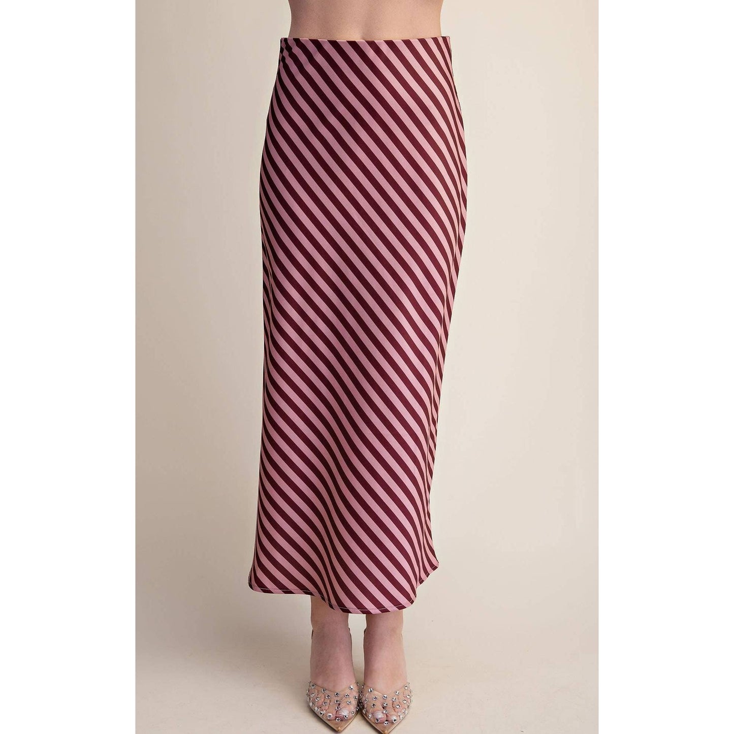 A woman wearing a high-waisted, midi-length skirt with diagonal burgundy and cream stripes, paired with light pink embellished heels, against a plain beige studio background.
